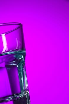 The water in glass on lilac background at studio. Vivid bright colored lighting. Trendy in 2018 Ultra Violet Light Bulb. Art decoration with tone of mystic color