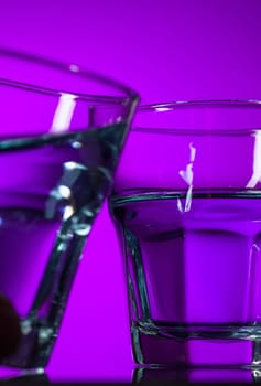 The water in two glasses on lilac background at studio. Vivid bright colored lighting. Trendy in 2018 Ultra Violet Light Bulb. Art decoration with tone of mystic color