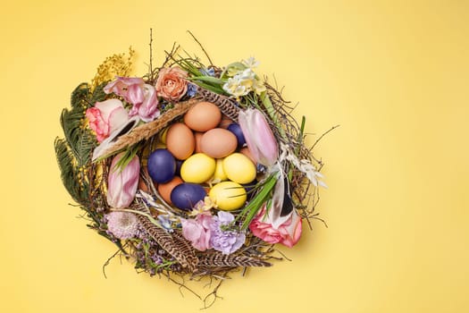 Easter card. Painted Easter eggs in nest on yellow table background. Top view of easter decoration. Happy easter concept