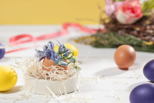 Beautiful easter table setting composition. A row of lilac and yellow color eggs on white wooden table background. Happy Easter greeting card. Side view