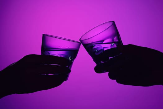 Two wine stuffed glasses and female and male hands at studio. Vivid bright colored lighting. Trendy in 2018 Ultra Violet Light Bulb. Art decoration. concept of toast
