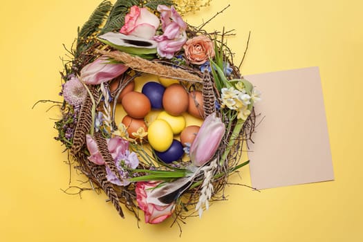 Easter card. Painted Easter eggs in nest on yellow table background. Top view of easter decoration. Happy easter concept