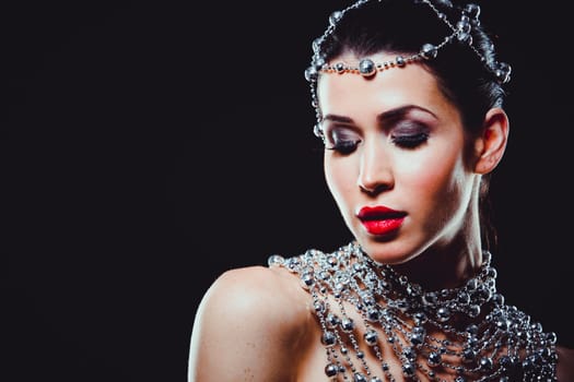 beautiful woman with dark makeup and red lipstick posing on black background. Wearing silver disco ball jewllery.