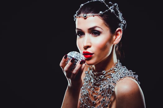 beautiful woman with dark makeup and red lipstick posing on black background. Wearing silver disco ball jewllery.