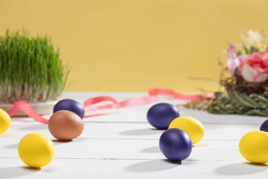Beautiful easter table setting composition. A row of lilac and yellow color eggs on white wooden table background. Happy Easter greeting card. Side view
