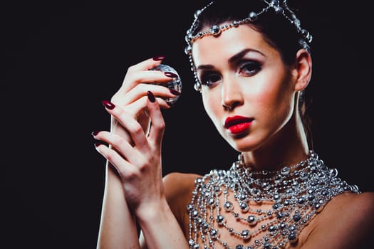 beautiful woman with dark makeup and red lipstick posing on black background. Wearing silver disco ball jewllery.