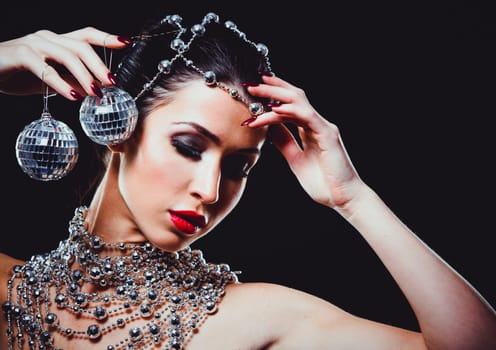 beautiful woman with dark makeup and red lipstick posing on black background. Wearing silver disco ball jewllery.