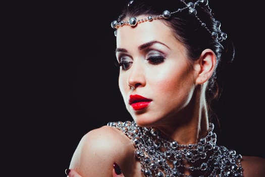 beautiful woman with dark makeup and red lipstick posing on black background. Wearing silver disco ball jewllery.