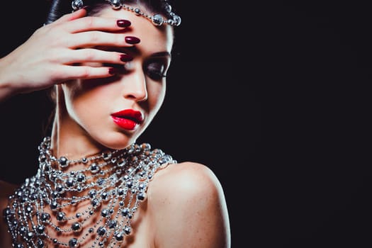 beautiful woman with dark makeup and red lipstick posing on black background. Wearing silver disco ball jewllery.