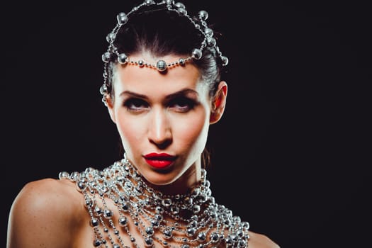 beautiful woman with dark makeup and red lipstick posing on black background. Wearing silver disco ball jewllery.