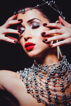 beautiful woman with dark makeup and red lipstick posing on black background. Wearing silver disco ball jewllery.