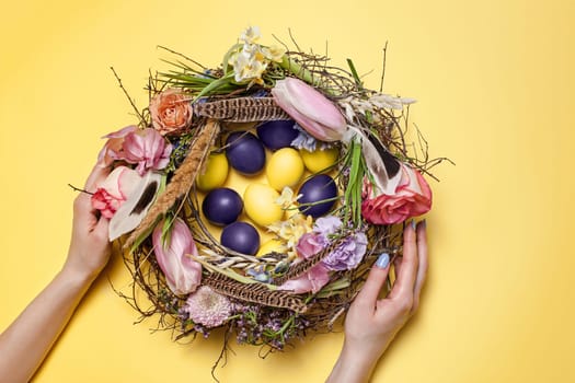 Easter card. Painted Easter eggs in nest on yellow table background. Top view of easter decoration. Happy easter concept