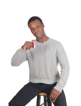 A handsome young African American man sitting in a gray sweater.and holding up his new credit card, isolated for white background.