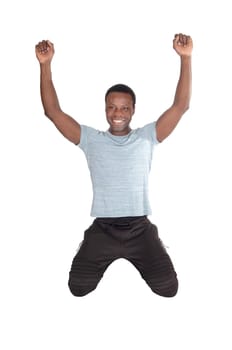 A young handsome African American man kneeling on the floor with.his fists and smiling of victory and success, isolated over white.
