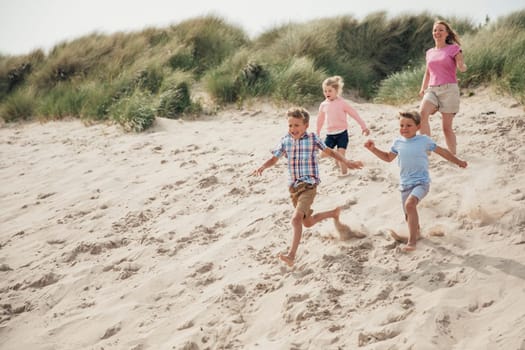 Family having fun running down the sand dunes at the beach while on holiday at the seaside.