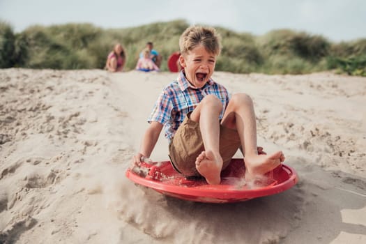 Young boy sliding down a sand dune while his family wait at the top.