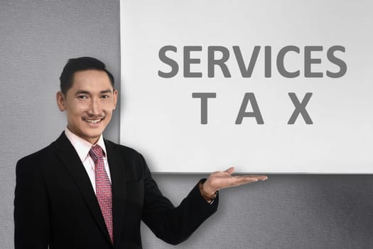 Young asian businessman standing beside whiteboard with service tax message. Goods and services tax concept