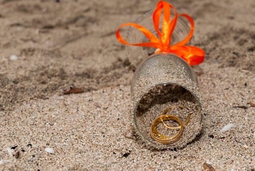 Two wedding ring inside a glass with a orange ribbon on the sand