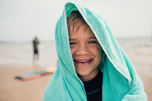 Little boy wrapped in a towel after surfing at the beach.