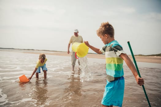 Rear view of little boys playing in the sea. Their grandad is standing close by watching over them.