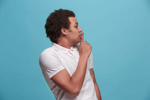 Secret, gossip concept. Young man whispering a secret behind his hand. Businessman isolated on trendy blue studio background. Young emotional man. Human emotions, facial expression concept.