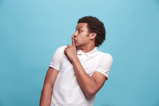Secret, gossip concept. Young man whispering a secret behind his hand. Businessman isolated on trendy blue studio background. Young emotional man. Human emotions, facial expression concept.