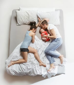 Top view of happy funny family with one newborn child in bedroom. Enjoying being together. Happy family in bed. Top view. Emotions concept. Morning after sleep. Family lifestyle. happy parents concept