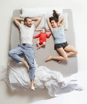 Top view of happy funny family with one newborn child in bedroom. Enjoying being together. Happy family in bed. Top view. Emotions concept. Morning after sleep. Family lifestyle. happy parents concept