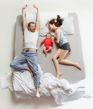 Top view of happy funny family with one newborn child in bedroom. Enjoying being together. Happy family in bed. Top view. Emotions concept. Morning after sleep. Family lifestyle. happy parents concept
