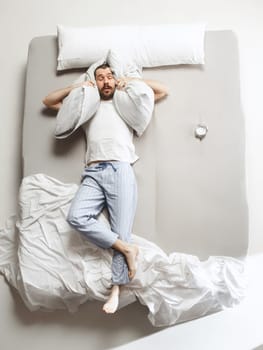 Top view photo of young man sleeping in a big white bed. Emotions concept. Morning after sleep. Happy man on the bed. alarm clock and unwillingness to wake up