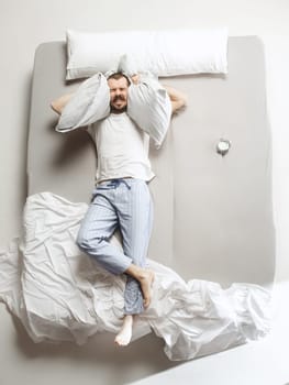 Top view photo of young man sleeping in a big white bed. Emotions concept. Morning after sleep. Happy man on the bed. alarm clock and unwillingness to wake up