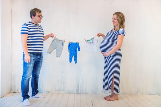 Young couple: pregnant woman and man holding baby clothes