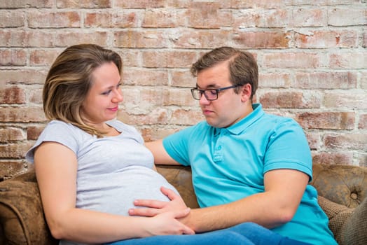 Beautiful pregnant woman and man sitting near brick wall