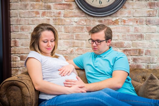 Happy pregnant woman and man sitting near brick wall