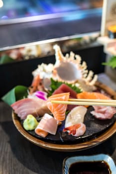 Closeup a slice of selective focus salmon sashimi with chopsticks in the Japanese restaurant near the chef bar and blurred sashimi set behind