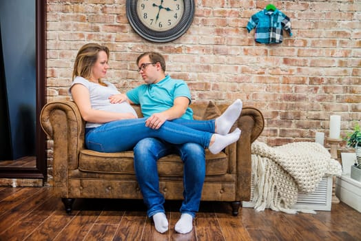 Beautiful pregnant woman and man sitting near brick wall