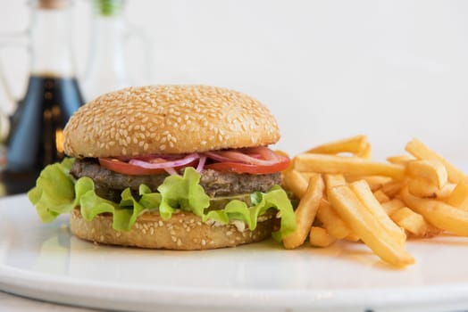Tasty classical burger with fried potato on white table