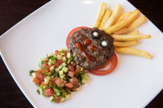 Funny meat cutlet face with french fries as hair and cutted vegetables for children menu