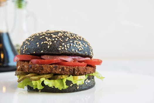 Black burger with beef meat cheese lettuce onion, tomato and sauce on white table