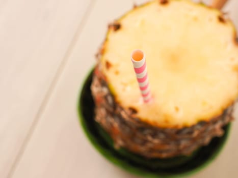 Fresh organic pineapple with a drinking straw on a wooden table, selective focus on the drinking straw, view from above