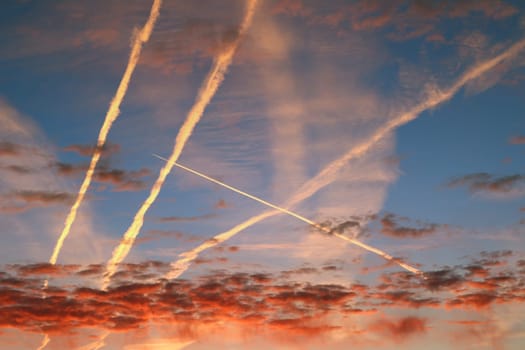Red morning clouds and streams of condensed vapor on the sky