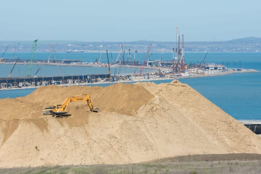 Taman, Russia - 15 April 2017: A huge pile of soil in the foreground, and the bend of the bridge under construction across the Kerch Strait in the background, as of April 2017