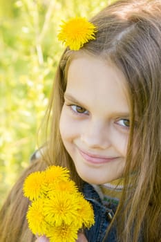 Portrait of a happy eight year old girl with dandelions in hands, against a background of green foliage