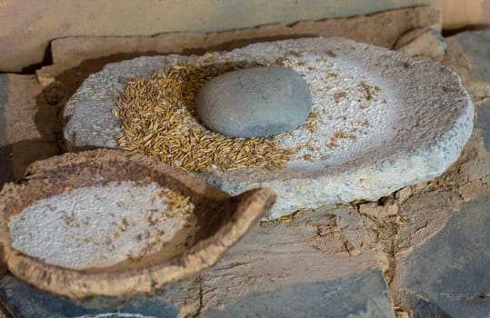 Jaen, Spain - December 29th, 2017: Neolithic era hand mill stone with barley and flour bowl made of cork. Selective focus. Jaen Museum