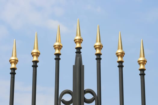 Wrought iron spikes of a gate, with a blue sky background