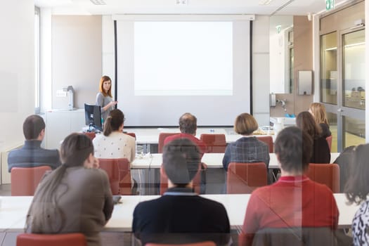 Speaker giving presentation in lecture hall at university. Participants listening to lecture and making notes. Copy space for brand on white screen.