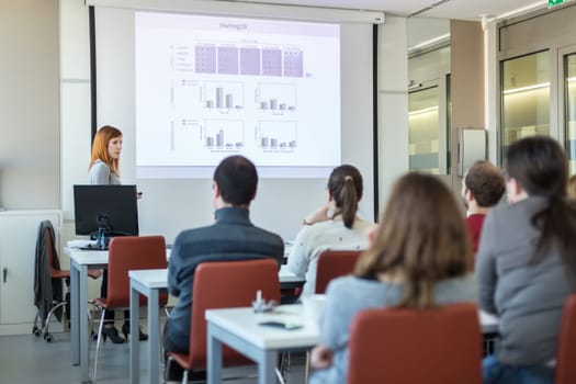 Female speaker giving presentation in lecture hall at university workshop. Audience in conference room. Rear view of unrecognized participant in audience. Scientific conference event.