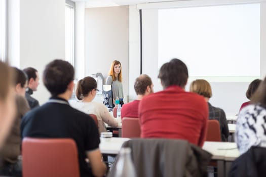 Female speaker giving presentation in lecture hall at university workshop. Audience in conference room. Rear view of unrecognized participant in audience. Scientific conference event.