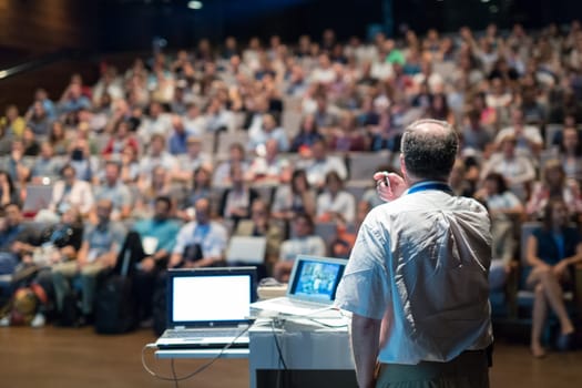 Speaker giving a talk on corporate business conference. Unrecognizable people in audience at conference hall. Business and Entrepreneurship event.