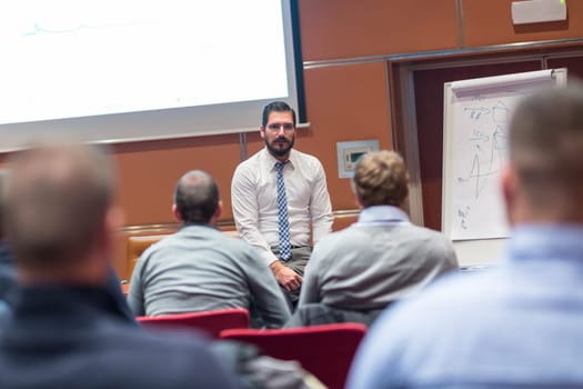 Skilled coach asks questions to participants of informal company business training. Audience in the conference room. Business and Entrepreneurship concept.